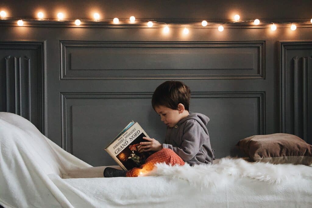 Ein kleiner Junge sitzt mit einem Buch auf einem Bett. 