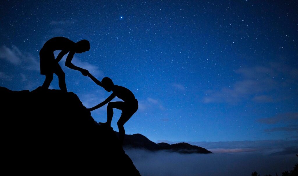 A man helps another man to climb a mountain. 