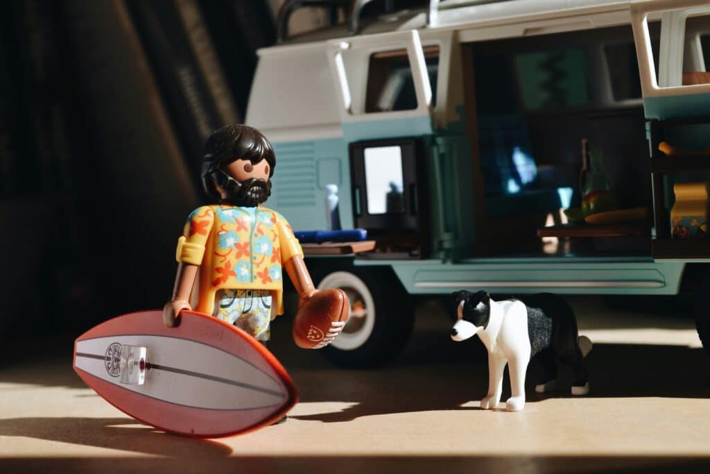A Playmobil figure with a surfboard next to a camping bus